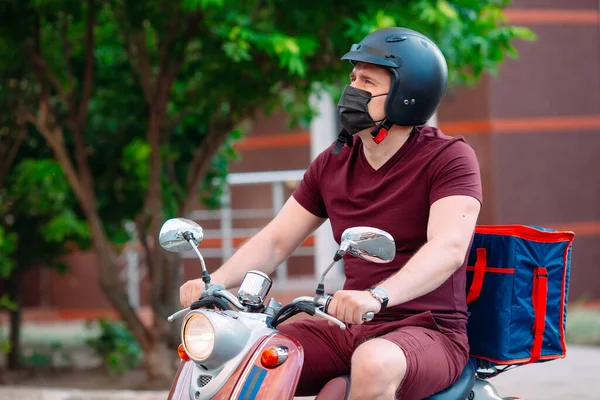 Scooter 'ın üzerinde kırmızı üniformalı teslimatçı çocuk ve hızlı giden izotermal yiyecek kutusu. Kafelerden ve restoranlardan ekspres yemek servisi. Moto scooter 'daki kurye yiyecek getiriyor..