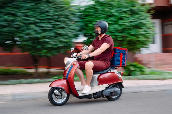 Scooter 'ın üzerinde kırmızı üniformalı teslimatçı çocuk ve hızlı giden izotermal yiyecek kutusu. Kafelerden ve restoranlardan ekspres yemek servisi. Moto scooter 'daki kurye yiyecek getiriyor..