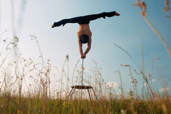 En man med atletisk uppbyggnad utför komplexa gymnastiska övningar på ett fält vid solnedgången. — Stockfoto