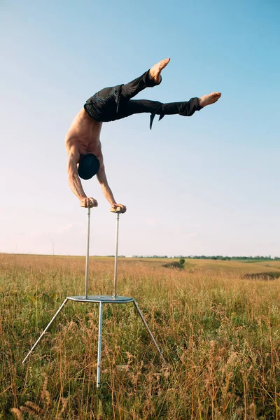 A man of athletic build performs complex gymnastic exercises in a field at sunset. — Stock Photo, Image