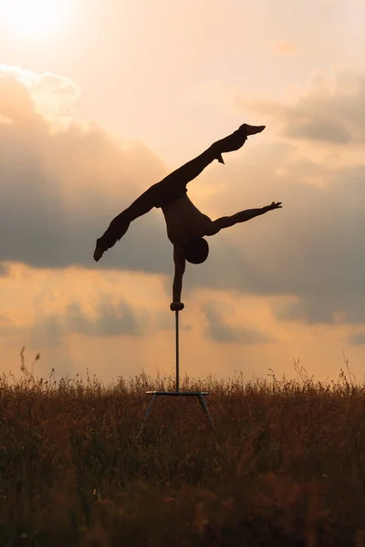 Um homem de construção atlética realiza exercícios ginásticos complexos em um campo ao pôr-do-sol. — Fotografia de Stock