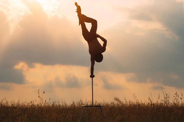 En man med atletisk uppbyggnad utför komplexa gymnastiska övningar på ett fält vid solnedgången. — Stockfoto
