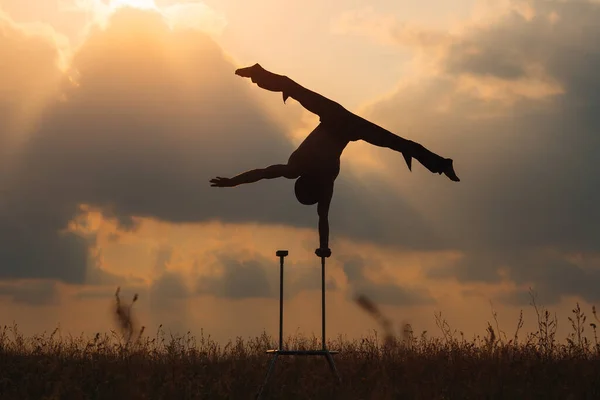 A man of athletic build performs complex gymnastic exercises in a field at sunset. — Stock Photo, Image