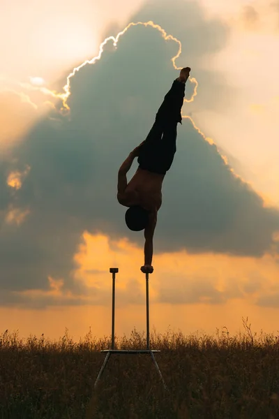 Un uomo di corporatura atletica esegue complessi esercizi ginnici in un campo al tramonto. — Foto Stock