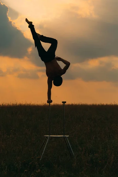 Człowiek o wysportowanej budowie wykonuje skomplikowane ćwiczenia gimnastyczne na polu o zachodzie słońca.. — Zdjęcie stockowe
