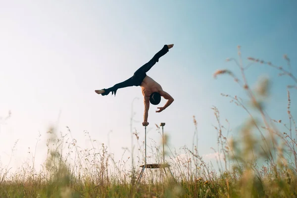 En man med atletisk uppbyggnad utför komplexa gymnastiska övningar på ett fält vid solnedgången. — Stockfoto