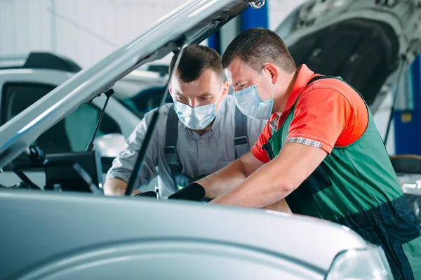 Mecânica em máscaras uniformes e protetoras trabalhar em uma oficina de carro. — Fotografia de Stock