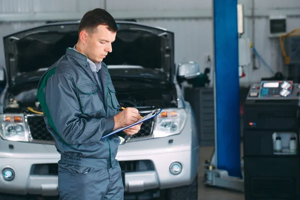 Mecánico mantener el registro del coche en el portapapeles en el taller de reparación. — Foto de Stock