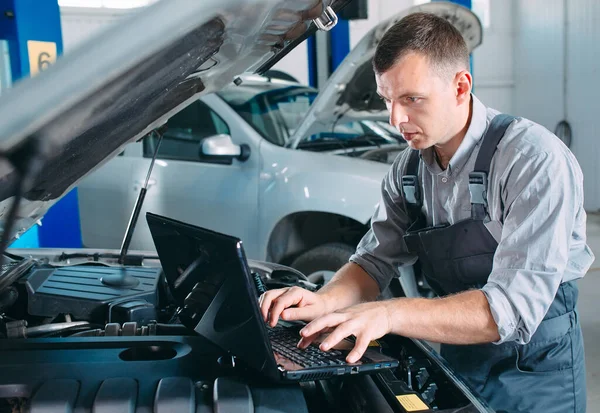 Araba tamircisi, tamir ve onarım için araba motorlarının parçalarını teşhis etmek ve kontrol etmek için bir bilgisayar dizüstü bilgisayar kullanıyor.. — Stok fotoğraf