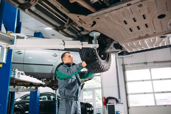 Auto sollevata in servizio automobilistico per il fissaggio, riparazioni operaie della ruota, — Foto Stock