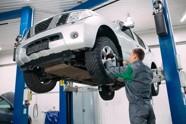 Auto sollevata in servizio automobilistico per il fissaggio, riparazioni operaie della ruota, — Foto Stock