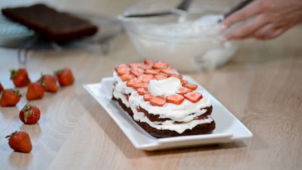 Donna mano mettere panna montata sulla torta di fragole . — Video Stock
