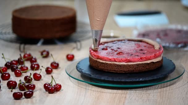 Unrecognizable female pastry cook squeezing chocolate cream on appetizing layer cake in kitchen. — Stock Video