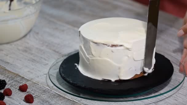 Nahaufnahme von Händen, die Buttercreme mit einem weißen Spachtel auf Schokoladenkuchen schmieren. — Stockvideo