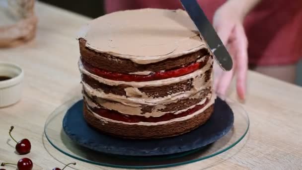 Irreconocible hembra pastelera apretando crema de chocolate en apetitoso pastel de capa en la cocina . — Vídeos de Stock