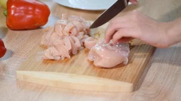 Nahaufnahme Frau schneidet Hühnerfilet mit einem Keramikmesser auf einem Holzbrett. Köchin schneidet rohe Hühnerbrust. — Stockvideo