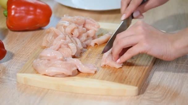 Nahaufnahme Frau schneidet Hühnerfilet mit einem Keramikmesser auf einem Holzbrett. Köchin schneidet rohe Hühnerbrust. — Stockvideo