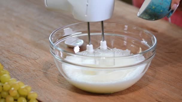 As mãos femininas adicionam um açúcar à tigela com claras de ovo chicotadas com misturador na mesa de madeira azul. Receita passo a passo de biscoitos merengue . — Vídeo de Stock
