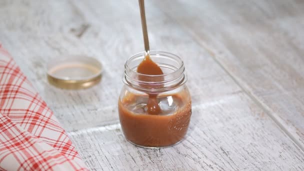 Zelfgemaakte gezouten karamel saus in pot op rustieke houten tafel achtergrond. — Stockvideo