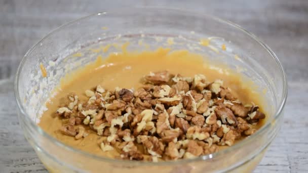 En kock i köket blandar i en glasskål med spatel. Lägg valnötter i smeten. — Stockvideo