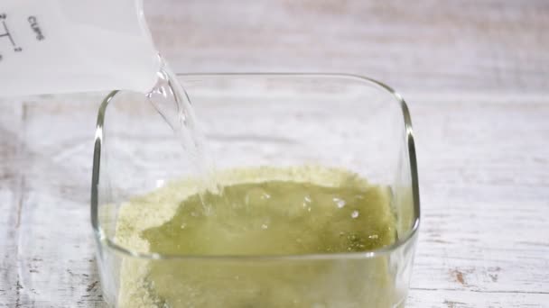 Gietend heet water. Groene gelei maken. Roer de gelei in de glazen kom. — Stockvideo