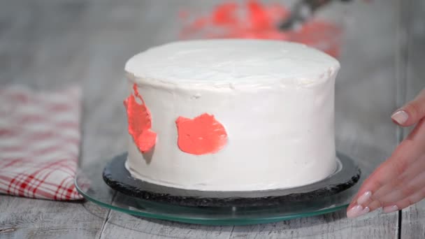 La mano del confitero unta la crema rosada en la torta blanca de la crema de la esponja del glaseado en el tocadiscos de madera en la cocina de la panadería, cerca . — Vídeos de Stock