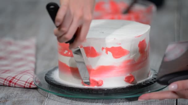 La mano del confitero unta la crema rosada en la torta blanca de la crema de la esponja del glaseado en el tocadiscos de madera en la cocina de la panadería, cerca . — Vídeo de stock