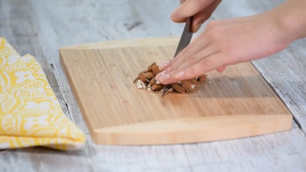 Vrouwelijke handen snijden amandelen op houten snijplank. — Stockvideo