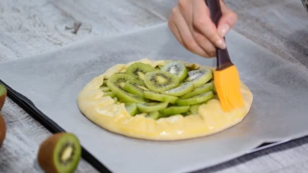 Het proces van het koken van een galette met verse kiwi. Vrouwelijke chef-kok smeren de bakkerijproducten met een ei — Stockvideo