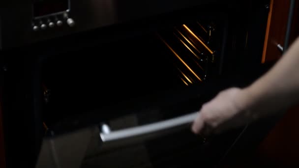 Una mano femminile mette una teglia con pane fatto a mano all'interno di un forno di casa . — Video Stock