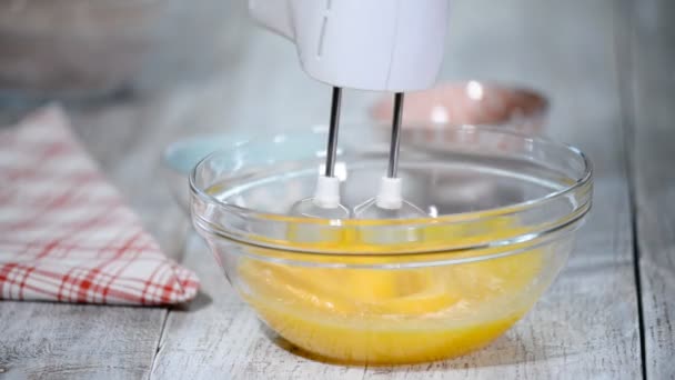Шеф-повар бьет яйца в миску с ручным миксером, чтобы сделать торт. Торт ингредиенты на столе . — стоковое видео