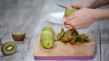 Bir kadın bir ahşap zemin üzerinde bir bıçakla kivi kabuğu temizler.