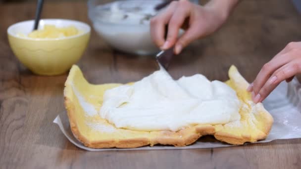 Close up hands of unrecognizable confectioner spreading cream on sponge cake when making swiss roll at home. — Stock Video