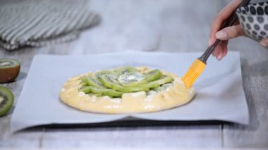 Bir Galette'ye taze kivi ile pişirme süreci. Kadın şef yağlamak bir yumurta ile ekmek yapım ürünleri.