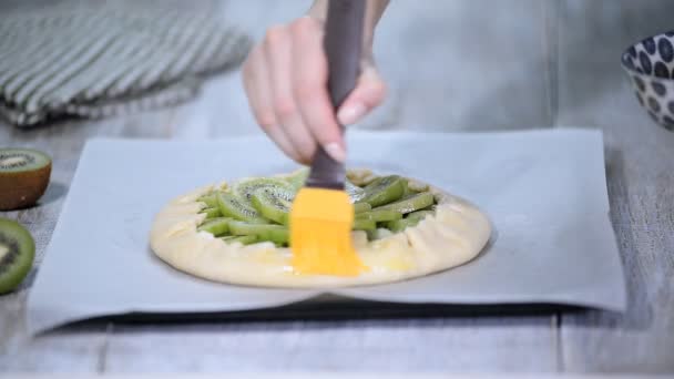 Le processus de cuisson d'une galette avec kiwi frais. Femme chef lubrifier les produits de boulangerie avec un oeuf . — Video