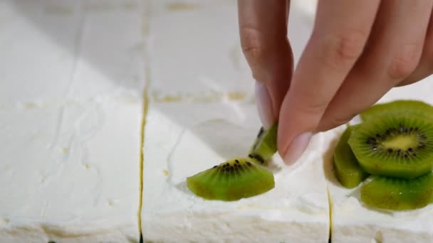 Weibliche Hand legt die Kiwi oben auf den Kuchen. — Stockvideo