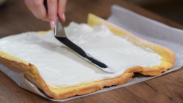 Gros plan, mains de confiseur méconnaissable étaler la crème sur le gâteau éponge lors de la fabrication rouleau suisse à la maison . — Video