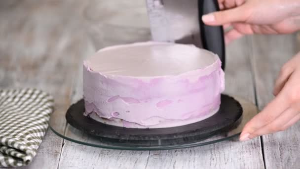 Процес прикраси торта фіолетовим кремом. Кондитер прирівнює вершки для печива за допомогою шпателя для випічки . — стокове відео