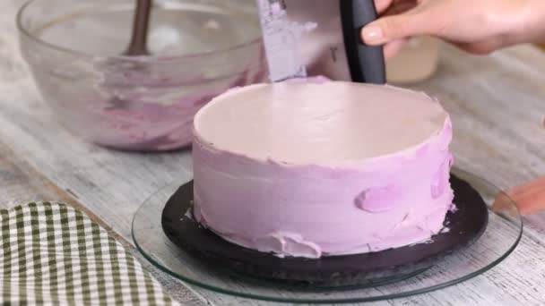 Proces zdobení dort s fialovým krém krytem. Cukrář se rovná sušenka krémem pomocí špachtle těsto.