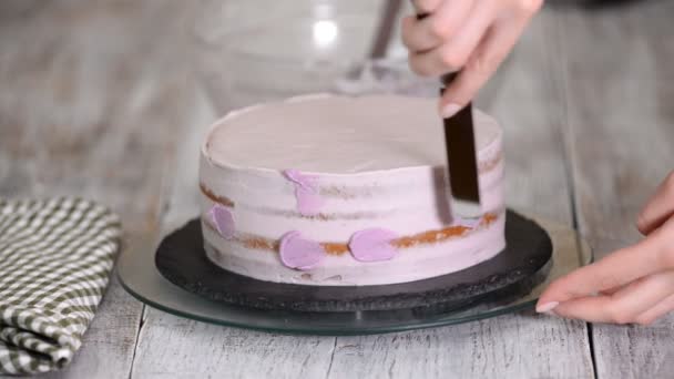 Процесс украшения торта фиолетовым кремовым покрытием. Кондитер приравнивает крем для печенья с помощью кондитерской лопатки . — стоковое видео