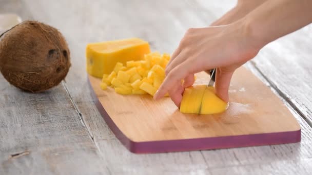 Female Chefs hands slice mango on wooden cutting board. Summer healthy vegan fruits salad on green bokeh background outdoor. — Stock Video