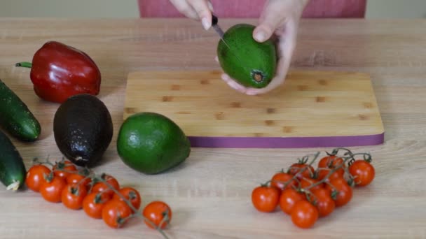 Jonge vrouw bezuinigingen avocado op snijplank op tafel close-up. — Stockvideo