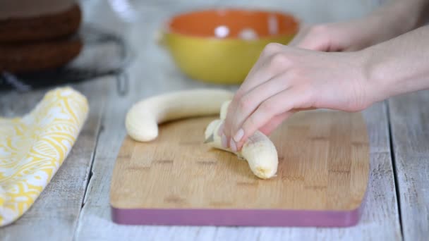 Close-up on woman cutting banana on cutting board. On a wooden table on a cutting board, a woman slicing a banana with knife. — Stock Video
