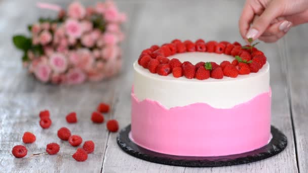 Close view donna mette foglie di menta per decorare la parte superiore bianca crema di torta biscotto rosa in piedi sul piatto — Video Stock