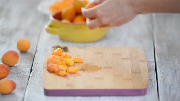 Close-up de mãos femininas cortando damascos com uma faca em uma tábua de corte. Cozinhar alimentos vegetarianos . — Vídeo de Stock