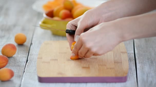 Közeli fel a női kéz vágó sárgabarack egy késsel a vágódeszka. Főzés vegetáriánus ételek. — Stock videók