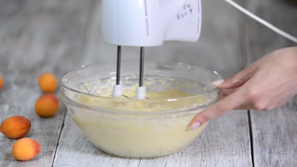 Mani femminili che mescolano la pasta con un frullatore per torta in una boccia su una cucina di legno — Video Stock