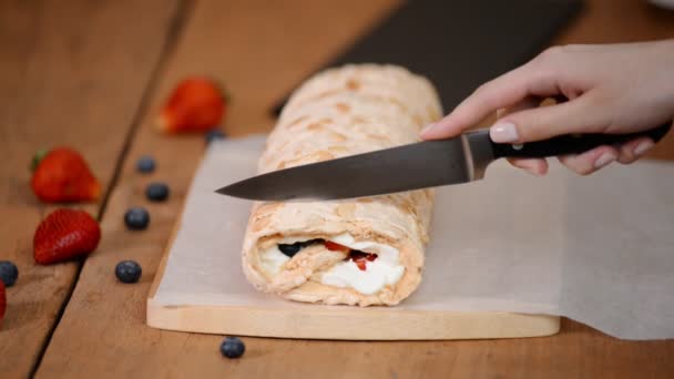 Meringue roll is versierd met bessen op een houten plank. Chef snijdt meringue rollade op houten snijplank — Stockvideo
