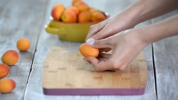 Close-up de mãos femininas cortando damascos com uma faca em uma tábua de corte. Cozinhar alimentos vegetarianos . — Vídeo de Stock