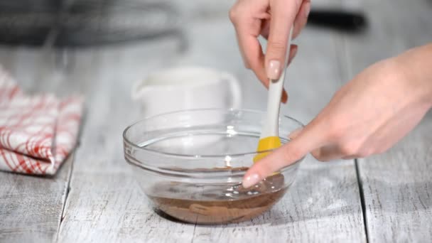 Пекарь перемешивает жидкий шоколад с глазурью в стеклянной чаше — стоковое видео